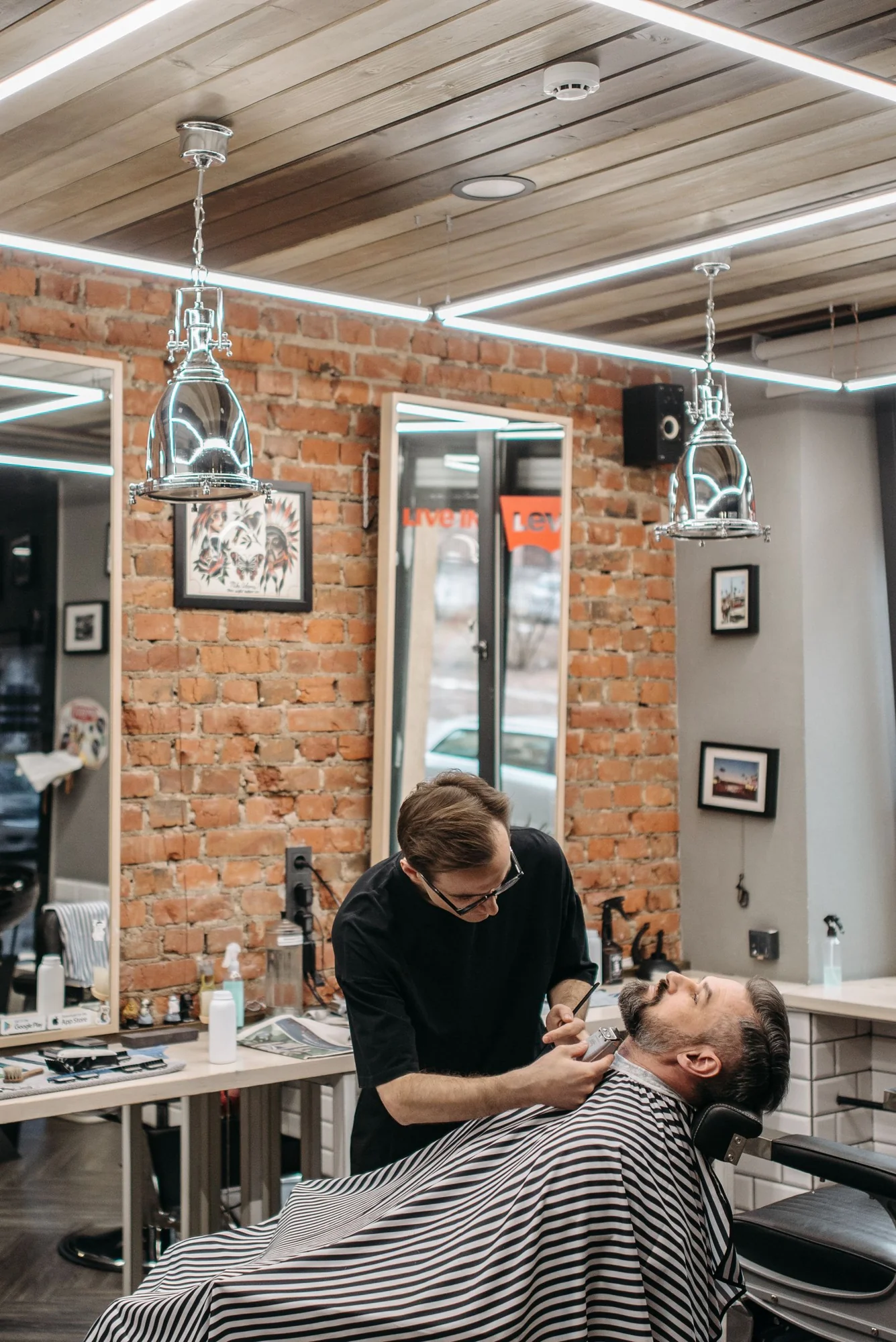 Barber carefully attending to a seated customer in a bright brick-walled salon