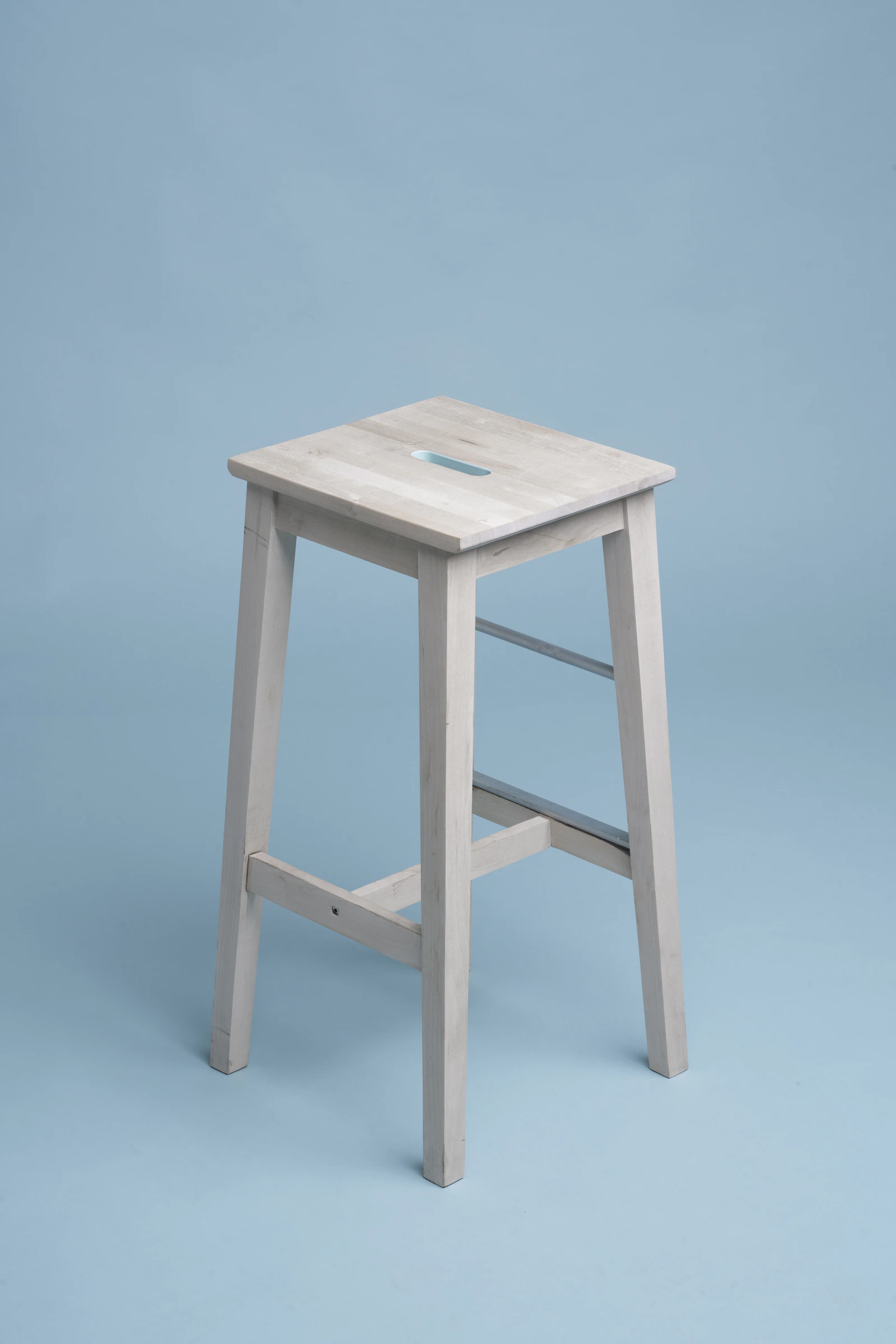 A simple white timber stool against a blue backdrop