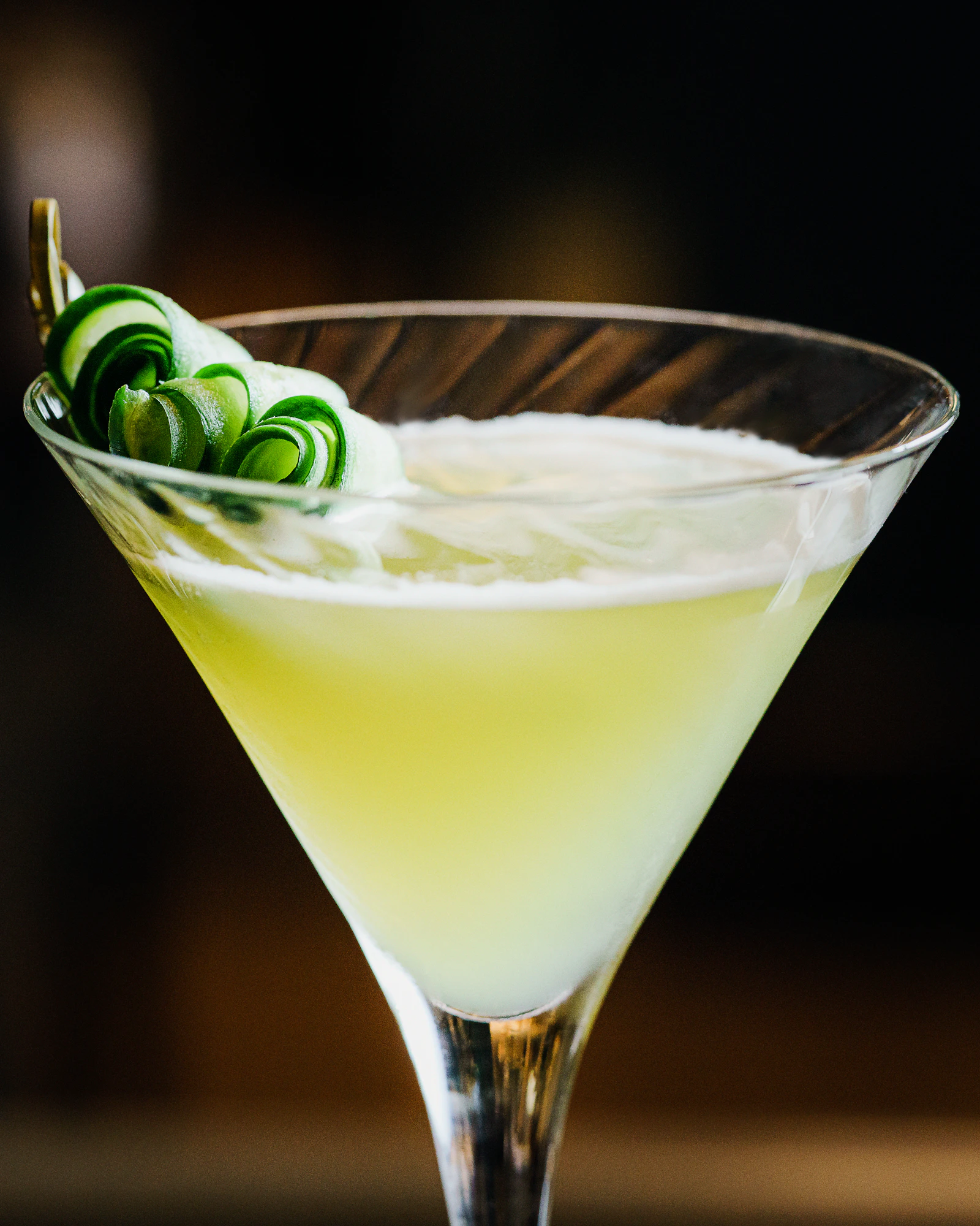 A pale cocktail with a cucumber garnish