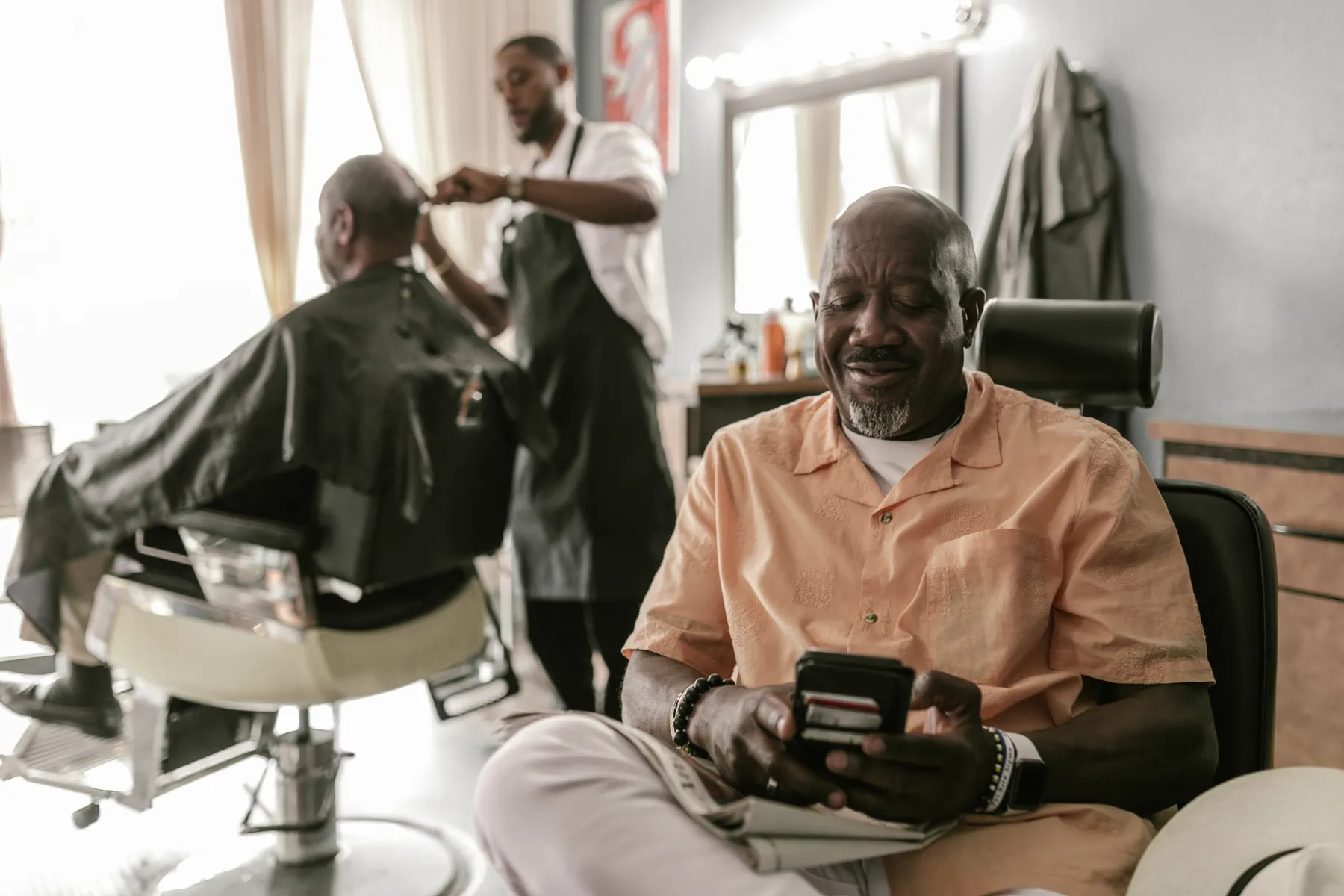 Seated man waiting in a warm barbershop while a barber works in the background