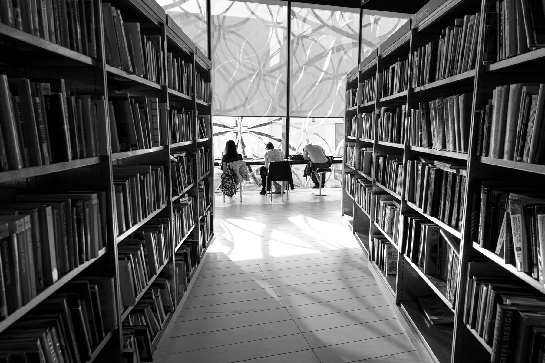 People reading at a table beyond shelves in a black-and-white library photograph