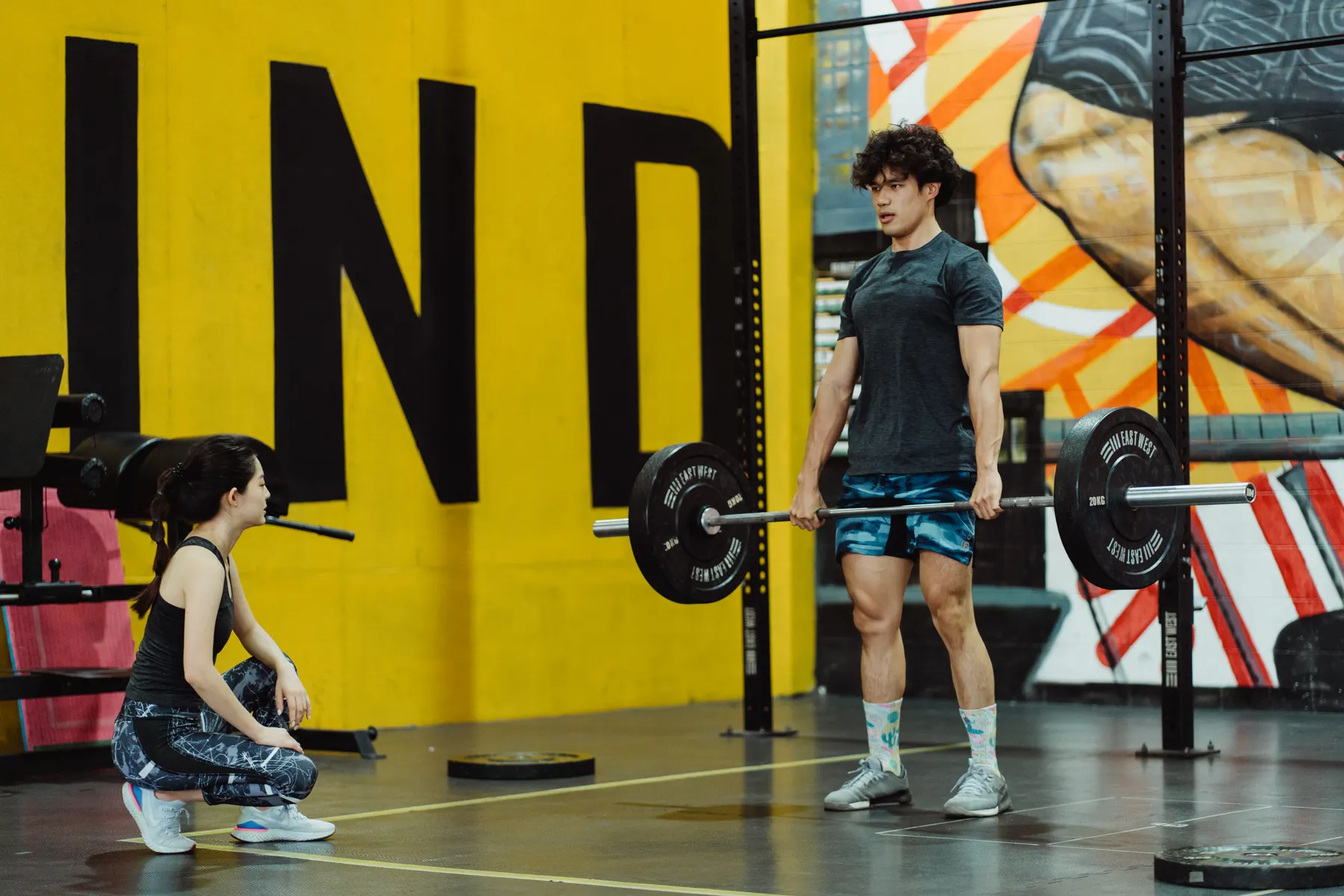 Man lifting a barbell while another person observes in a gym