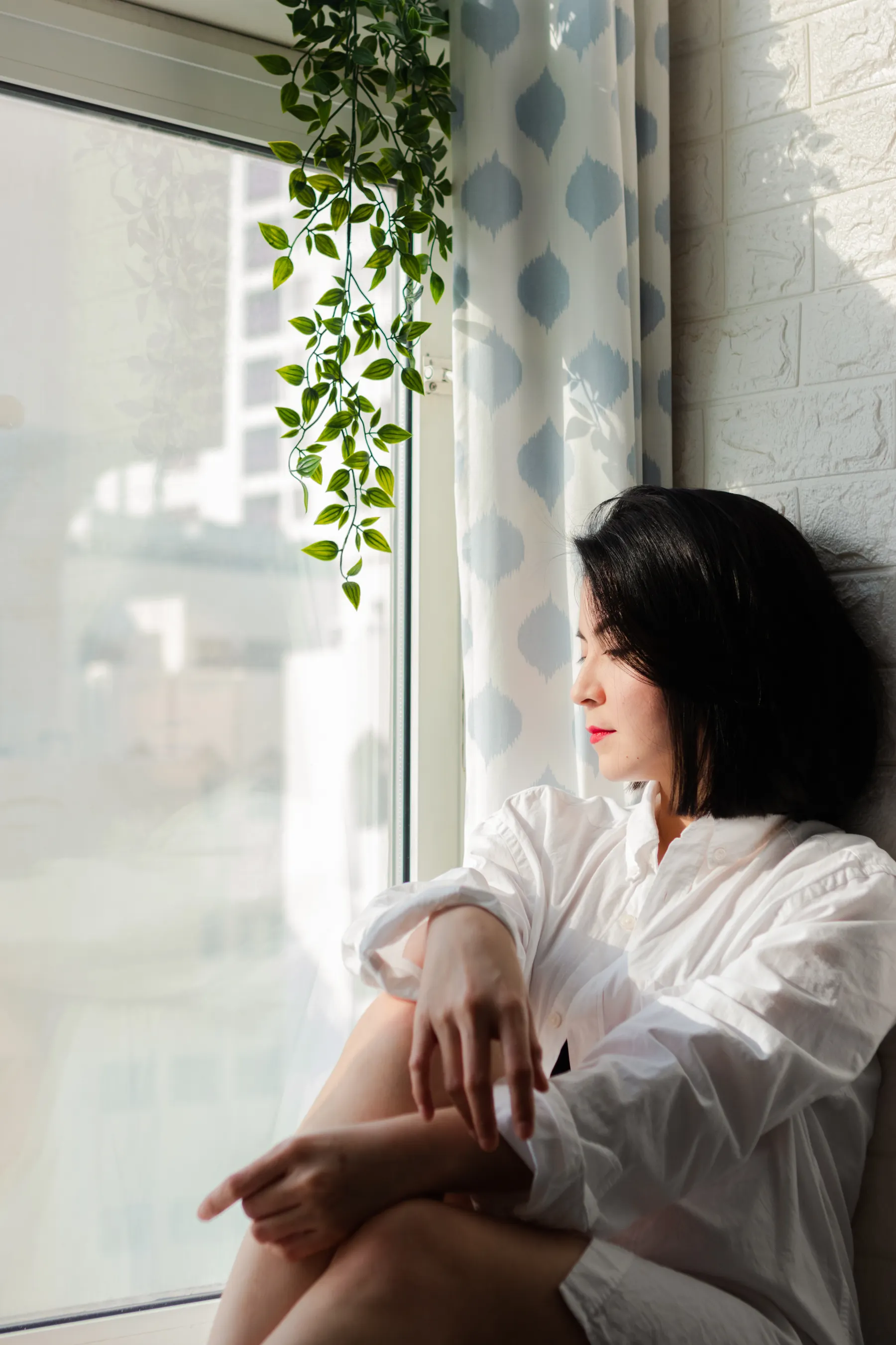 Woman in a white blouse photographed beside a window and plants