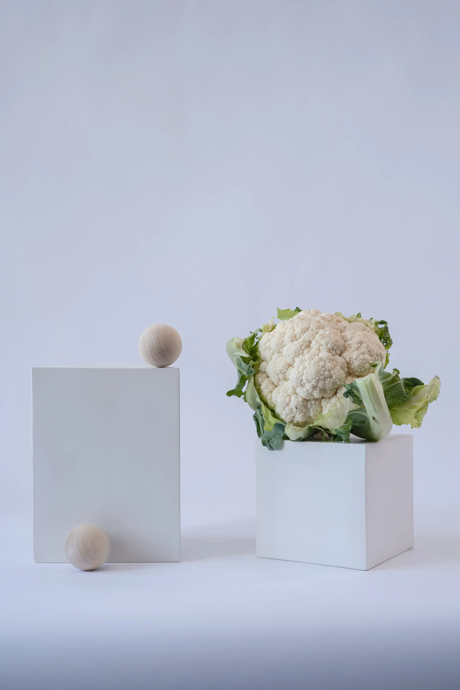 Cauliflower and wooden spheres arranged on white blocks in a still-life photograph