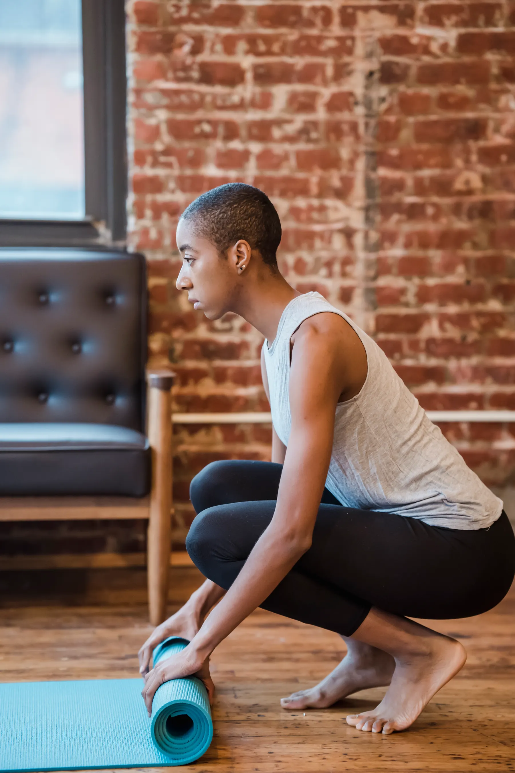 Woman unrolling a teal yoga mat in a brick studio