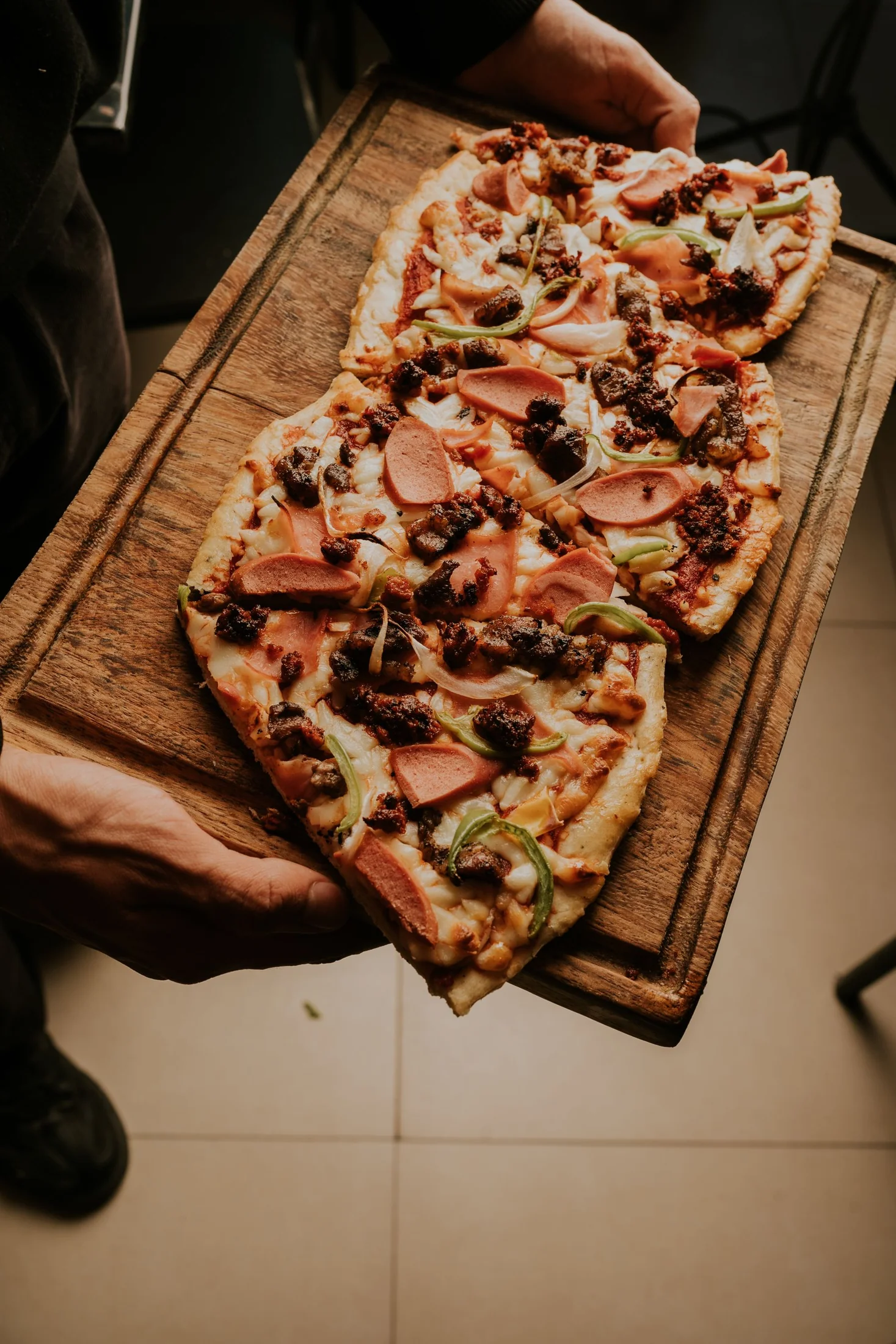 A long pizza with meat, peppers and onion on a wooden board