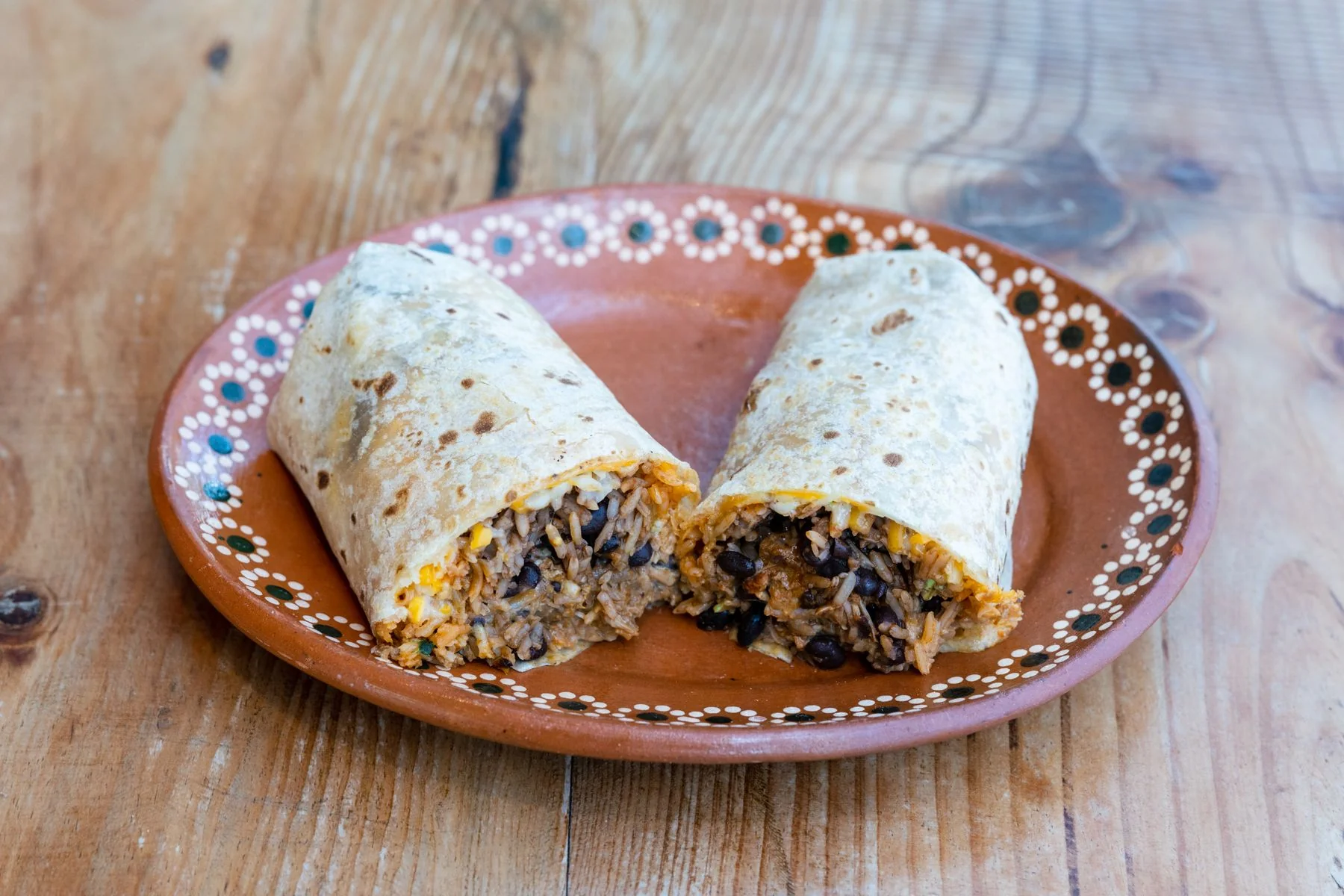 Two halves of a rice and bean burrito on a clay plate