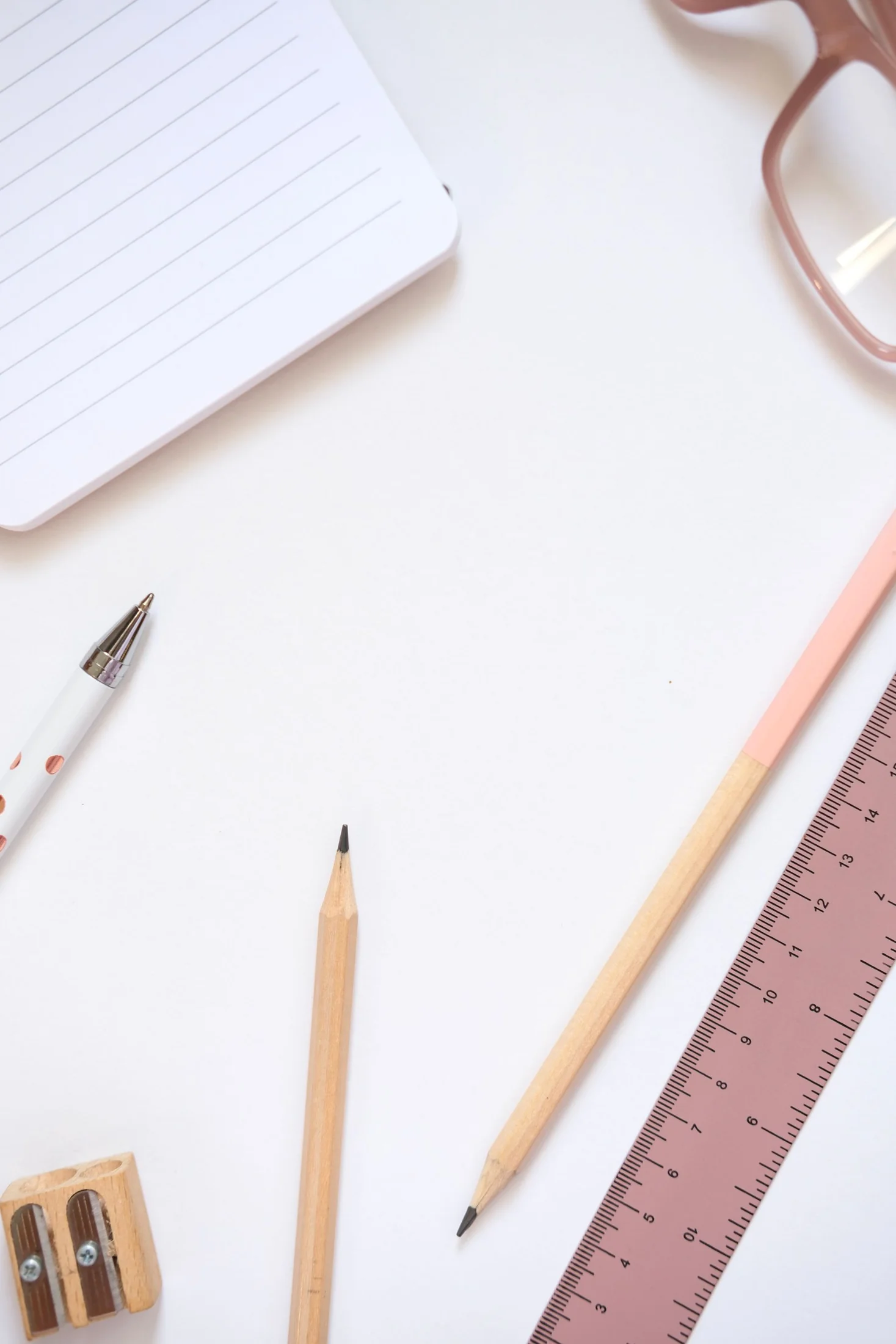Notebook, pencils and a pink ruler on a pale desk