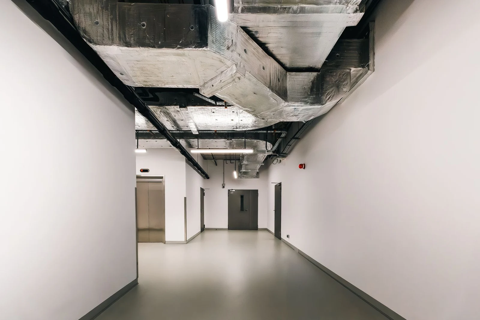 Exposed ventilation ductwork above a modern commercial hallway