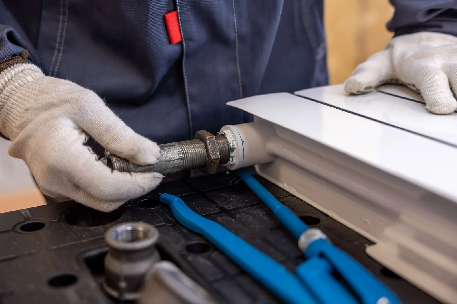 Gloved hands adjusting a radiator pipe fitting