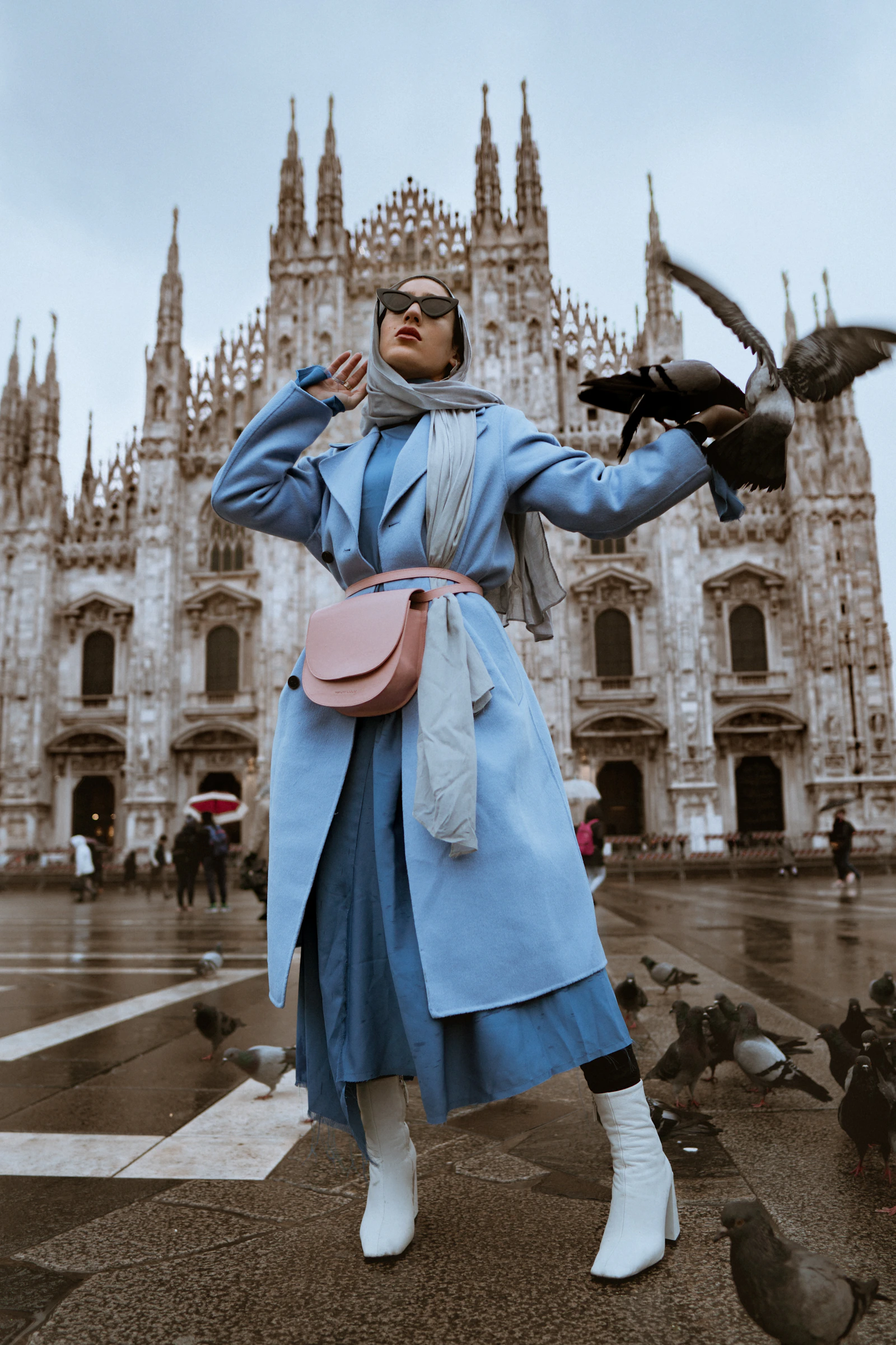 A woman wearing a tailored blue coat, silk scarf and a pink shoulder bag