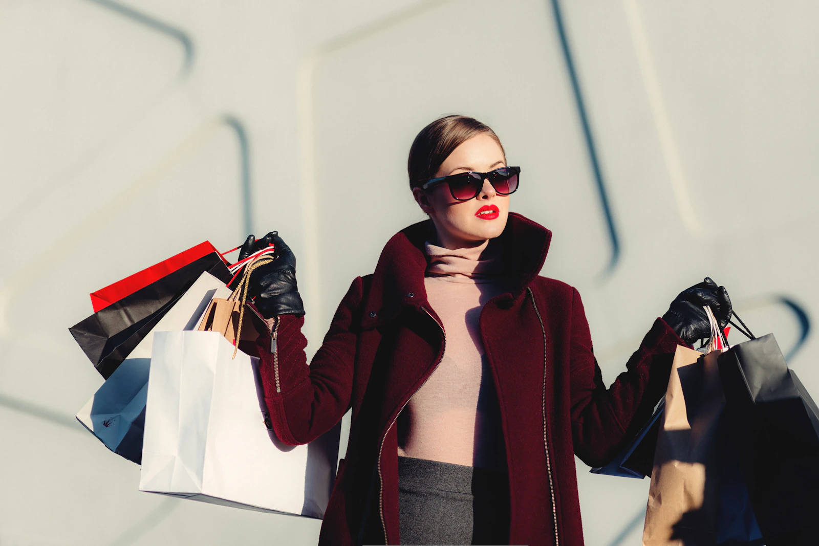 A woman in a burgundy coat and sunglasses carrying shopping bags