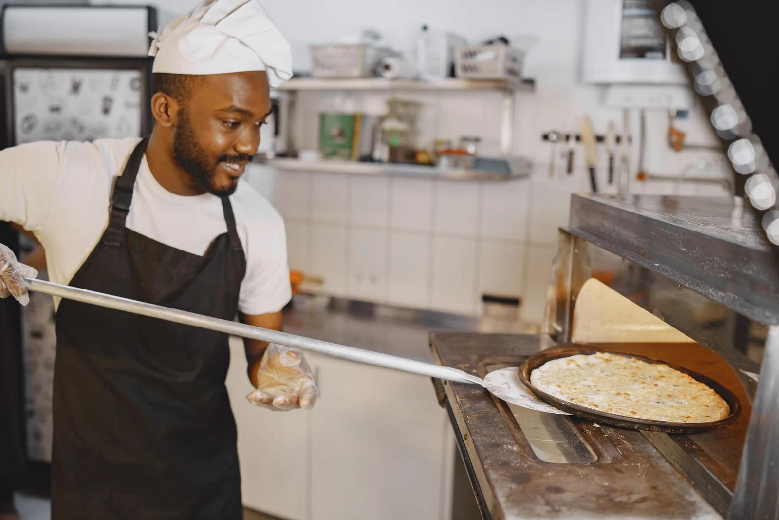 A cook lifting pizza from a commercial deck oven